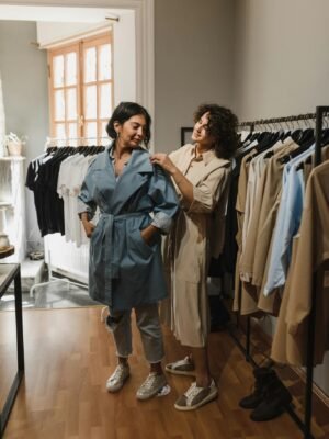 Two women shopping in a boutique, trying on stylish trench coat outfits.