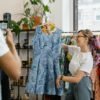 Woman happily showcasing a blue dress during a boutique sale, enhancing live shopping experience.