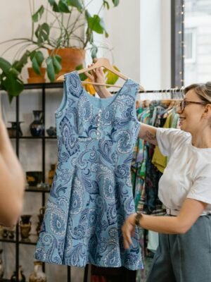 Woman happily showcasing a blue dress during a boutique sale, enhancing live shopping experience.