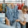 Woman inspecting a blue patterned dress in a retail clothing store. Fashion and shopping concept.
